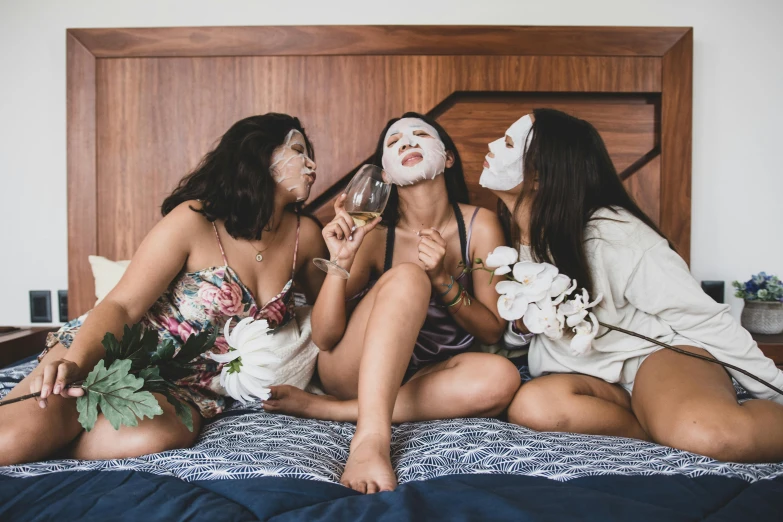 a group of women sitting on top of a bed, a photo, trending on pexels, flower mask, wine, white facepaint, three head one body