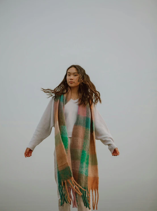 a woman standing on top of a sandy beach, trending on unsplash, happening, tartan scarf, draped in pink and green robes, on a cloudy day, young asian girl