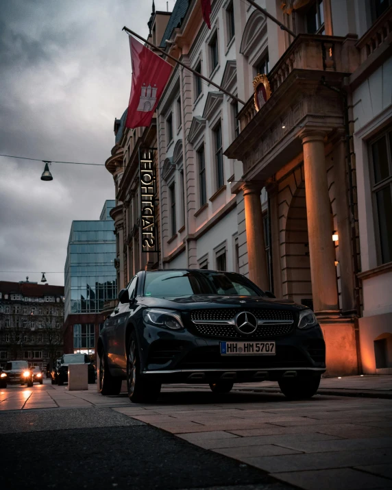 a black car driving down a street next to tall buildings, by Sebastian Spreng, pexels contest winner, mercedez benz, front lit, square, fashionable