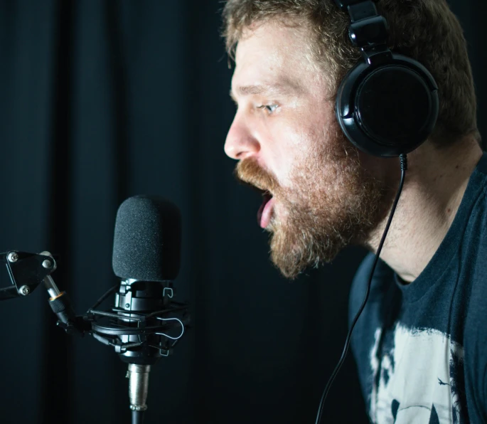 a man with headphones is singing into a microphone, inspired by Ásgrímur Jónsson, scruffy beard, promo image, unedited, in a studio