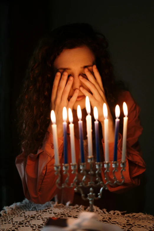 a woman sitting at a table with a menorah in front of her, pexels, renaissance, woman crying, multiple stories, teenage girl, holiday season