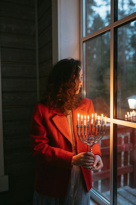 a woman holding a menorah in front of a window, pexels contest winner, seasonal, (1 as december, tall, human glowing