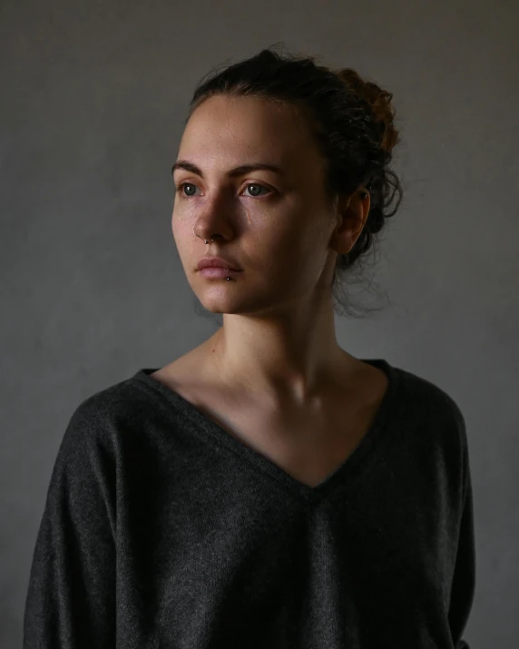 a woman standing in front of a gray background, inspired by irakli nadar, hyperrealism, somber lighting, wearing a dark sweater, queer woman, european woman photograph