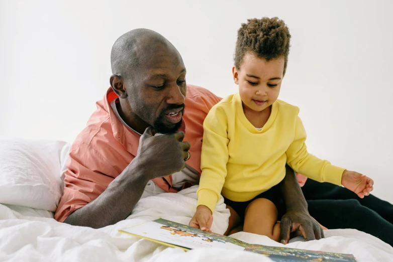 a man reading a book to a child on a bed, by Sam Charles, pexels contest winner, varying ethnicities, on a yellow canva, white background”, bald