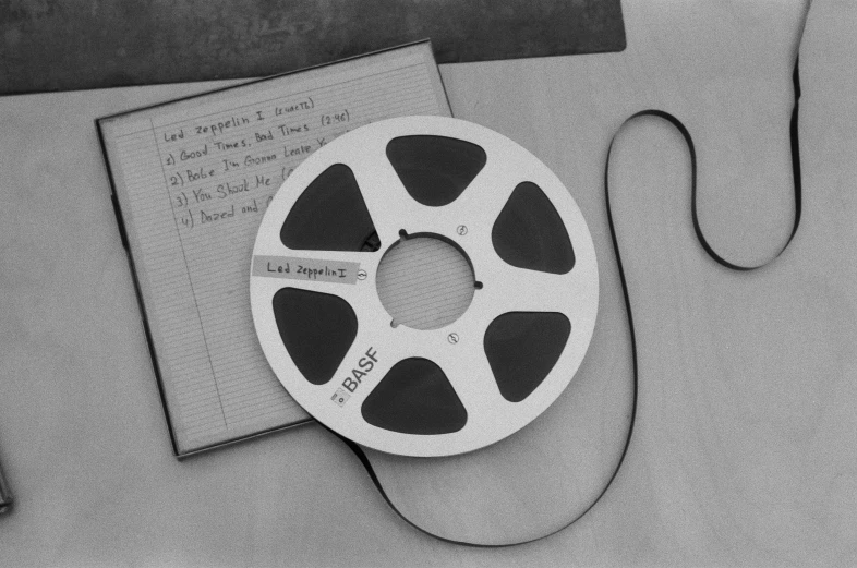 a black and white photo of a reel of film, an album cover, tape, a list cast, 1 9 8 5 photograph, digital image