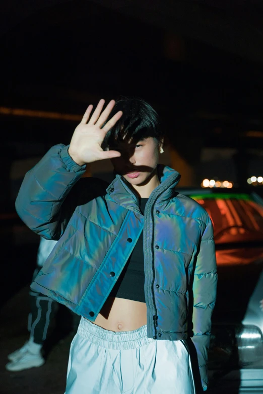 a woman standing in front of a car at night, an album cover, inspired by Elsa Bleda, trending on pexels, holography, model wears a puffer jacket, asian male, physical : tinyest midriff ever, waving