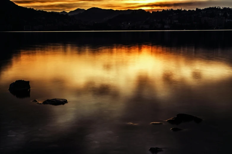 a sunset over a body of water with rocks in the foreground, pexels contest winner, romanticism, photo of zurich, dark yellowish water, lake reflection, today\'s featured photograph 4k