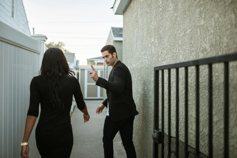 a man standing next to a woman in a black dress, by Ryan Pancoast, pexels contest winner, happening, standing outside a house, arguing, background image, chasing action scene