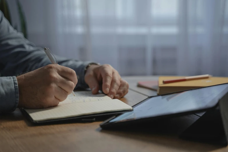 a man sitting at a desk writing on a piece of paper, by Carey Morris, pexels contest winner, full device, avatar image, holding notebook, wooden desks with books