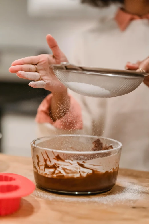 a woman mixing ingredients in a bowl on a kitchen counter, inspired by Gordon Browne, trending on pexels, process art, dough sculpture, caramel, partially cupping her hands, intimidating floating sand