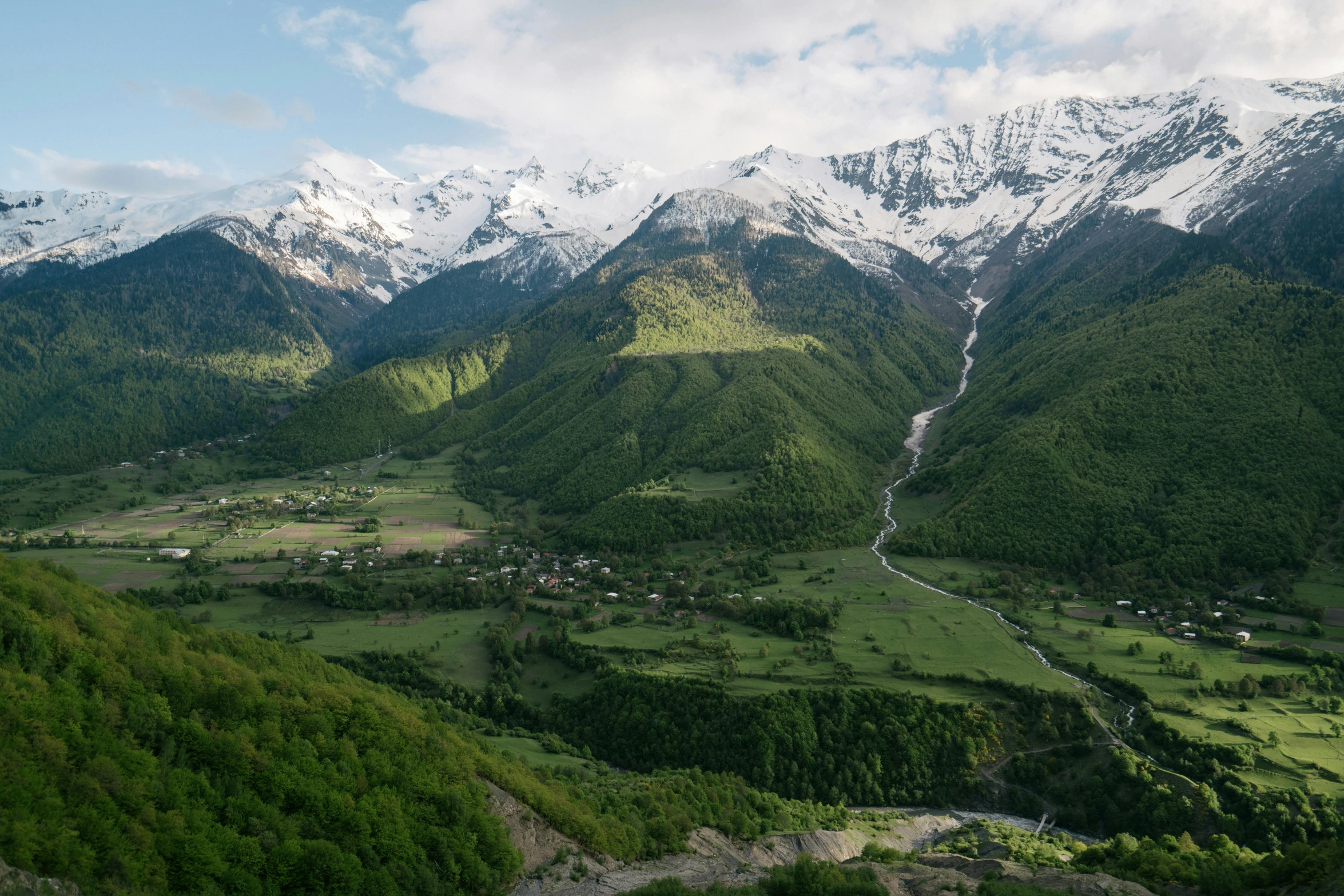 a view of a valley with mountains in the background, by Muggur, unsplash contest winner, hurufiyya, dezeen, lush green, snow capped mountains, southern european scenery