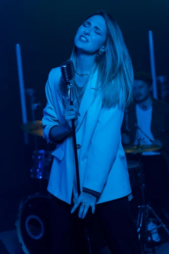a woman singing into a microphone on stage, an album cover, trending on pexels, photorealism, blue jacket, britt marling style 3/4, in a nightclub, cl
