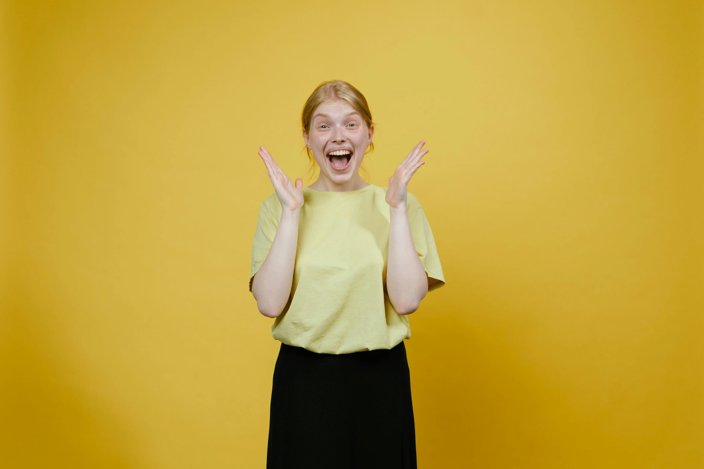 a woman standing in front of a yellow wall with her hands in the air, pexels contest winner, happening, round teeth and goofy face, very pale, avatar image, plain background