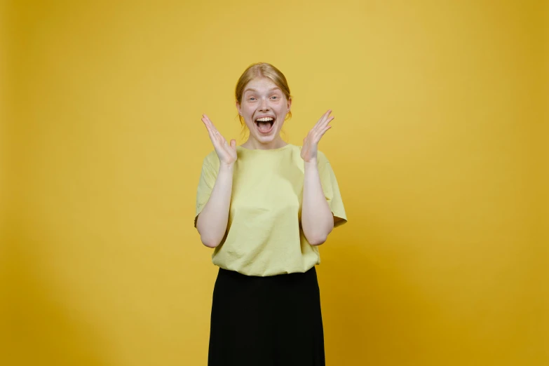 a woman standing in front of a yellow wall with her hands in the air, pexels contest winner, happening, round teeth and goofy face, very pale, avatar image, plain background
