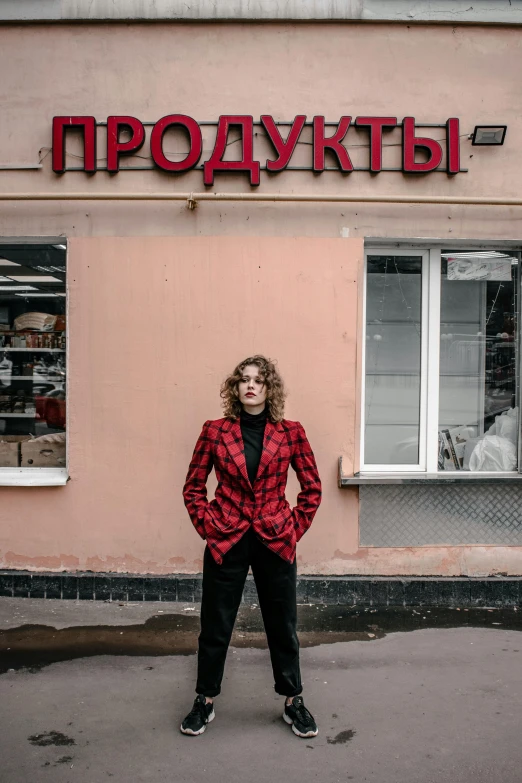 a woman standing in front of a store, by Julia Pishtar, pexels contest winner, russian style, androgyny, red and black suit, 🚿🗝📝