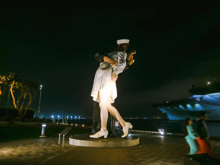 a couple of people that are standing in front of a statue, a statue, navy, during the night, nursing, standing on two legs