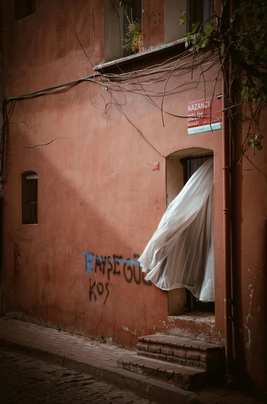 a white sheet hanging from the side of a building, a silk screen, pexels contest winner, graffiti, marrakech, cloak covering face, faded red colors, about to enter doorframe