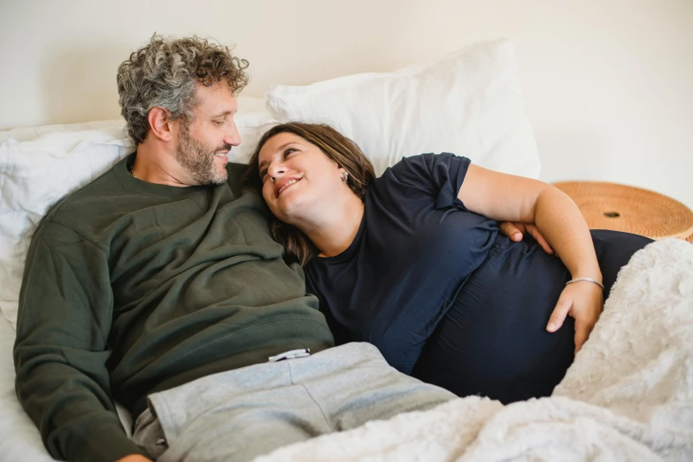 a man and woman laying in bed next to each other, pexels contest winner, happening, pregnant belly, smiling at each other, avatar image, casually dressed