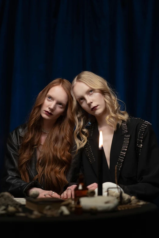 two women sitting at a table with candles, an album cover, unsplash, renaissance, long ginger hair, leather robes, siamese twins, pale skin and dark eyes