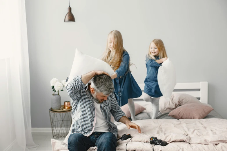 a man sitting on top of a bed next to a little girl, pexels contest winner, happening, families playing, bedhead, light grey backdrop, cushions