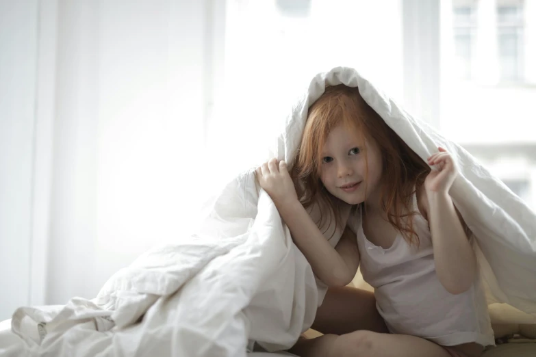 a little girl sitting on top of a bed under a blanket, pexels contest winner, figuration libre, ( redhead, dressed in a white t shirt, ad image, young girls
