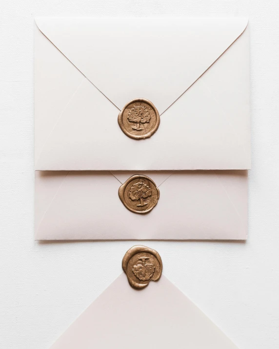 three envelopes with wax seals sitting on top of each other, by Emma Andijewska, letterism, light blush, miniature product photo, made of bronze, product image