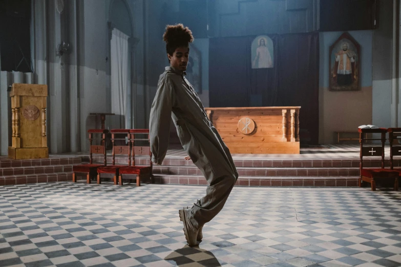 a person standing in a room with a checkered floor, an album cover, by Raphaël Collin, unsplash, visual art, scene set in a church, chappie in an adidas track suit, she is dancing, [ theatrical ]