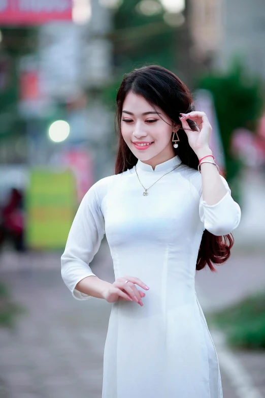 a woman in a white dress standing on a sidewalk, a picture, inspired by Ruth Jên, pexels contest winner, ao dai, wearing tight shirt, warm smile, square