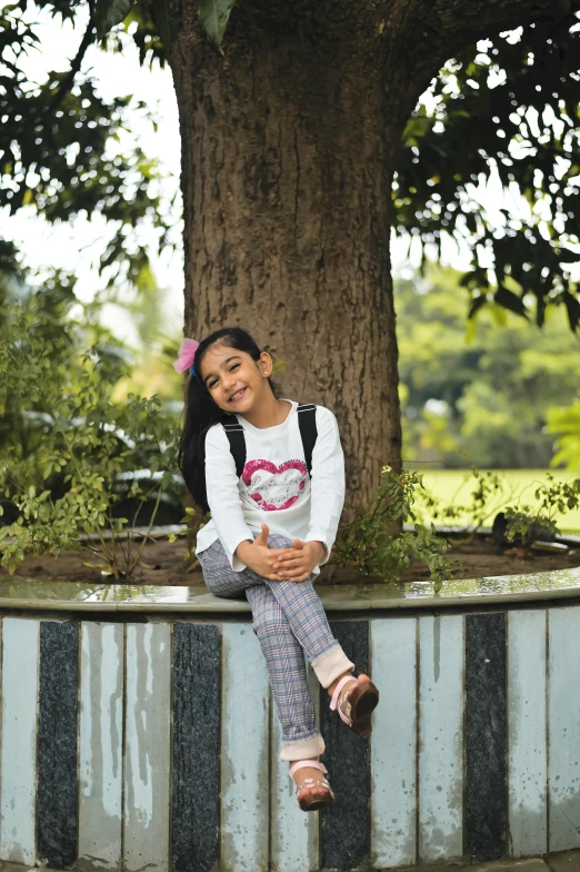 a girl sitting on a wall next to a tree, while smiling for a photograph, avatar image, for junior, vastayan