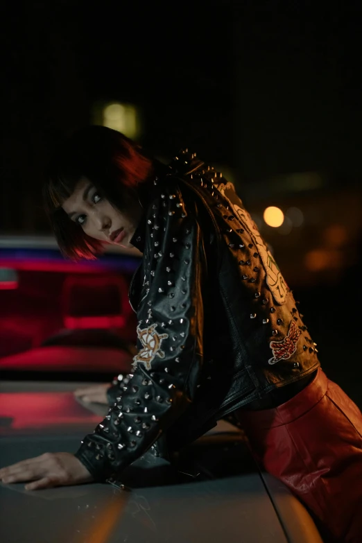 a woman leaning on the hood of a car, an album cover, inspired by Elsa Bleda, trending on pexels, photorealism, wearing studded leather, kiko mizuhara, high red lights, ( ( theatrical ) )