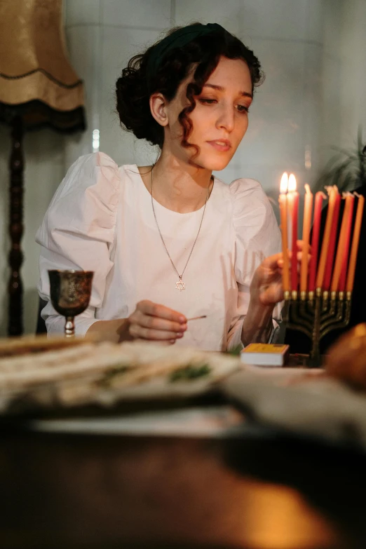 a woman sitting at a table with a menorah in front of her, pexels, renaissance, praying with tobacco, food stylist, gif, plating