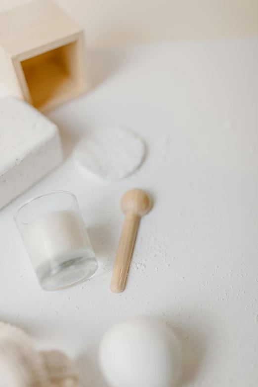 a couple of eggs sitting on top of a white table, flour dust spray, holding a wood piece, holding a candle holder, photoshoot for skincare brand