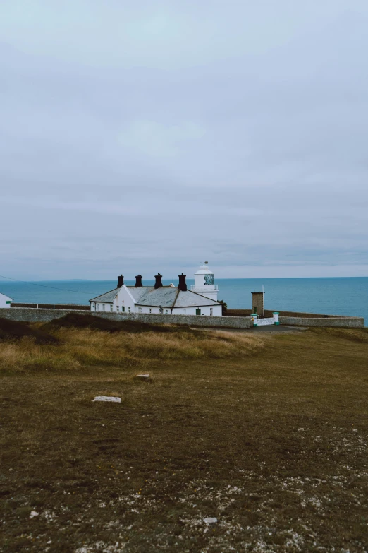 a lighthouse sitting on top of a hill next to the ocean, several cottages, low ultrawide shot, square, unsplash 4k