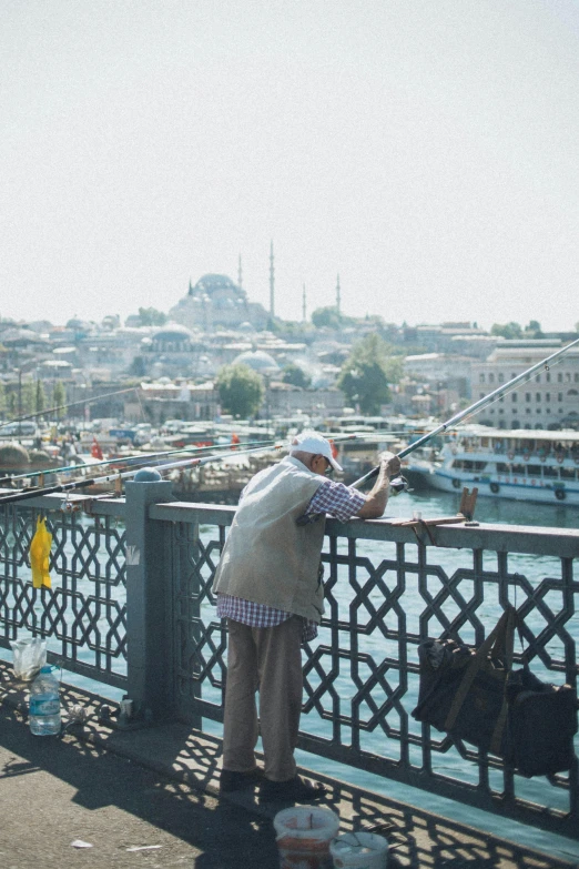 a man standing on top of a bridge next to a body of water, hurufiyya, fishing pole, istanbul, an elderly, movie filmstill