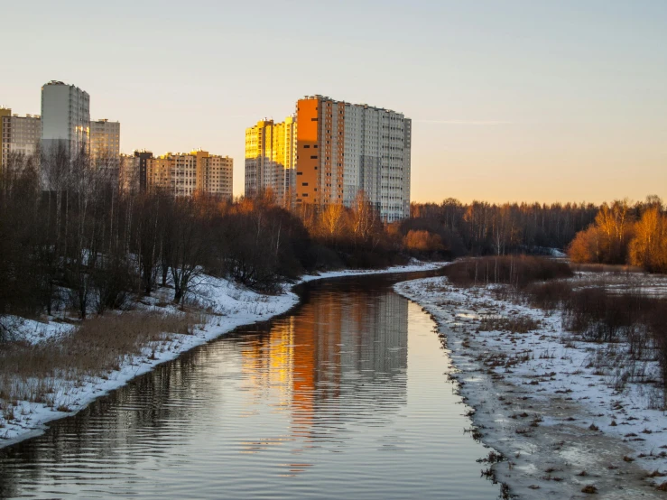 a river running through a city next to tall buildings, inspired by Alexei Kondratyevich Savrasov, pexels contest winner, hurufiyya, espoo, sparse winter landscape, golden hour 4k, today\'s featured photograph 4k