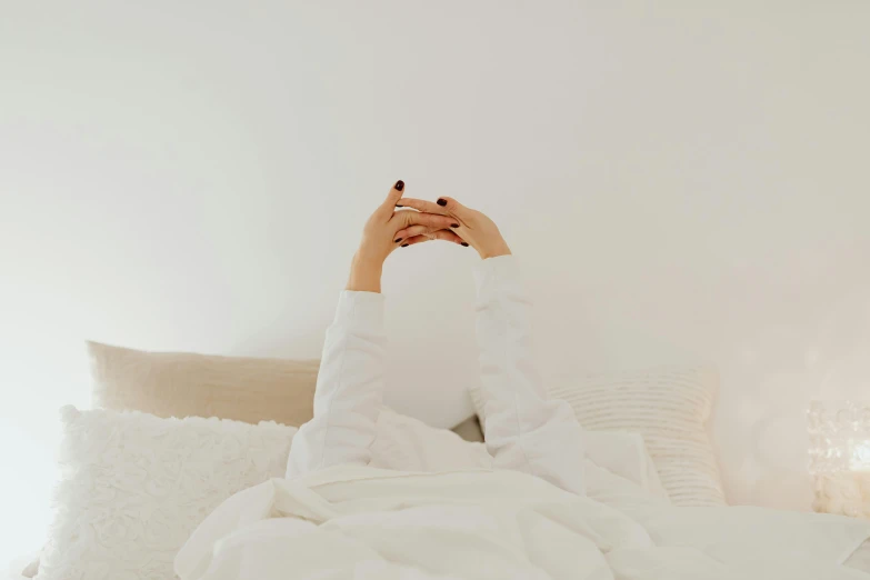 a woman laying on top of a bed under a blanket, inspired by Elsa Bleda, trending on pexels, aestheticism, holding his hands up to his face, white robes, flat minimalistic, sitting on a couch