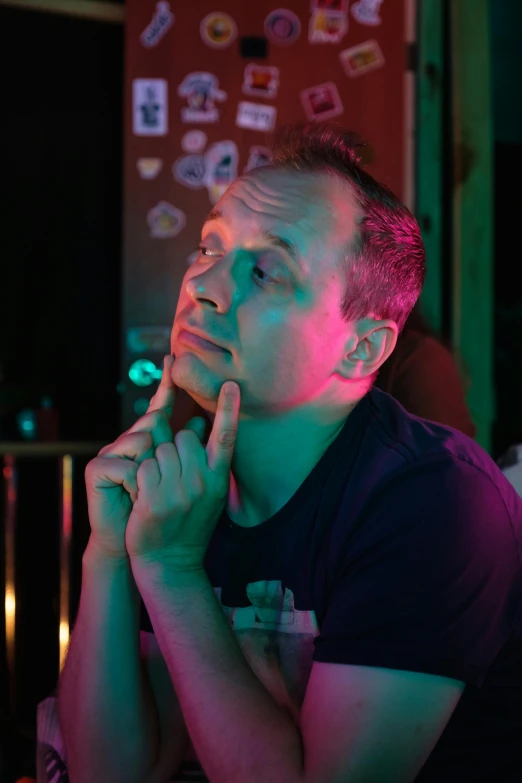 a man sitting at a table in a dark room, big forehead, thinking pose, flashing lights, soft chin