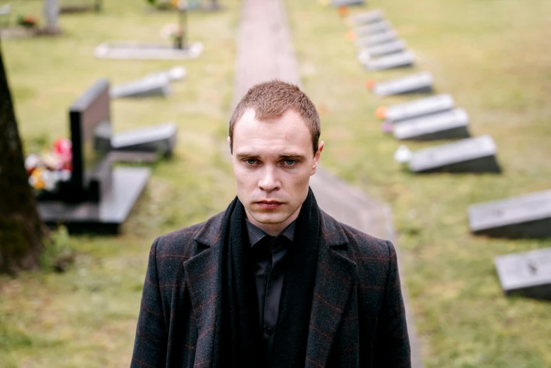 a man standing in front of a row of graves, an album cover, inspired by Oskar Lüthy, frank dillane, movie still 8 k, funeral, looking serious