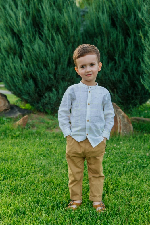 a young boy standing on top of a lush green field, wearing a linen shirt, award-winning style, pants, mateus 9 5