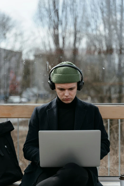 a man sitting on a bench with a laptop and headphones, an album cover, trending on pexels, serious face, russian academic, it's raining outside, human computer