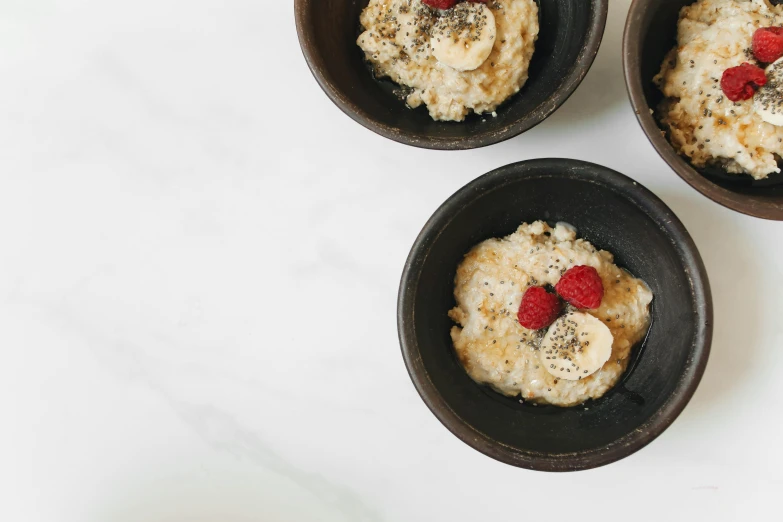 three bowls of oatmeal with bananas and raspberries, by Emma Andijewska, trending on unsplash, renaissance, background image, fine dining, high quality product image”