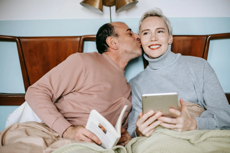 a man kissing a woman while sitting on a bed, a photo, trending on pexels, reading a book, two skinny old people, phone photo, non binary model