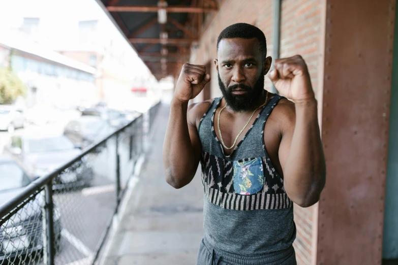 a man with a beard standing in front of a building, by Jessie Alexandra Dick, pexels contest winner, black arts movement, heroic muay thai stance pose, donald glover, boxing ring, shoulders up