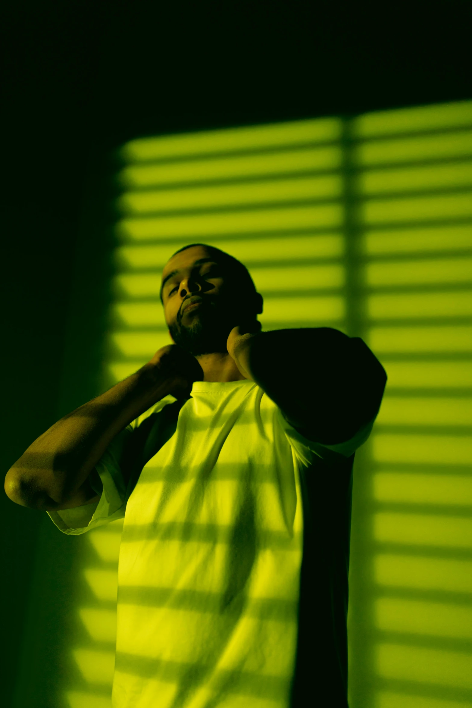 a man standing in front of a green wall, an album cover, pexels, realism, drake, yellow lighting, high shadow, ( ( theatrical ) )