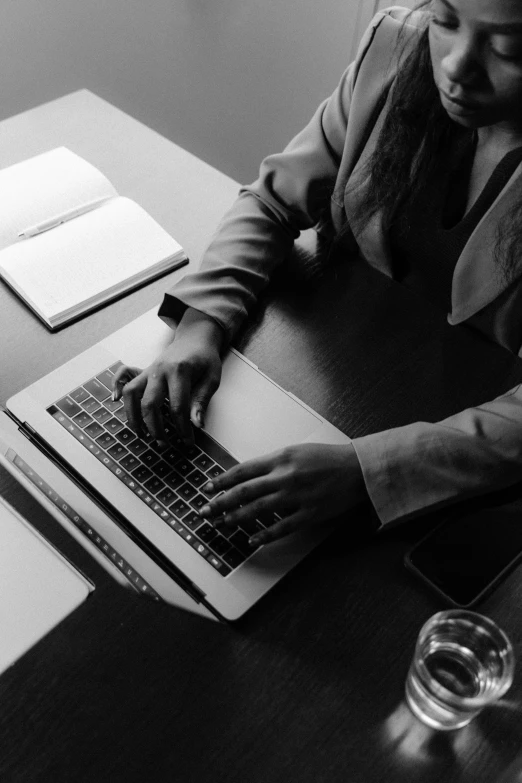 a man sitting at a table using a laptop computer, a black and white photo, by Carey Morris, pexels, computer art, business woman, lit from above, programming, email