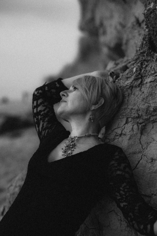 a black and white photo of a woman leaning against a tree, inspired by Ruth Brandt, unsplash, realism, silver haired, lying pose on stones, oceanside, profile pic