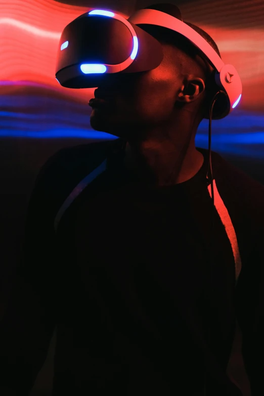 a man wearing a virtual reality headset in a dark room, pexels, afrofuturism, red and blue back light, promo image, dark. no text, with head phones