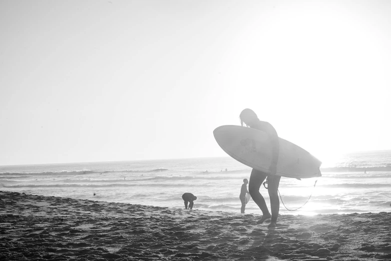 a man holding a surfboard on top of a sandy beach, a black and white photo, by Tom Bonson, pexels contest winner, sparkling in the sunlight, male and female, kailee mandel, people in beach