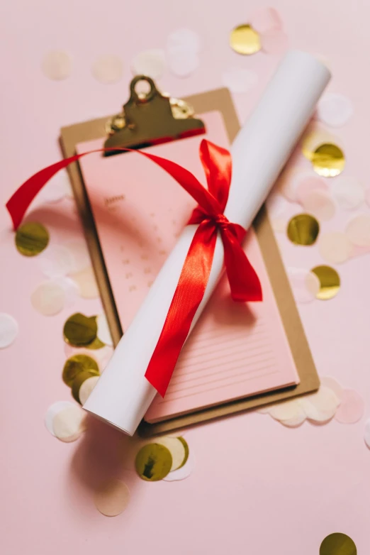 a diploma with a red ribbon on a pink background with confetti, a picture, by Julia Pishtar, pexels contest winner, happening, clipboard, wedding, scrolls, evening light