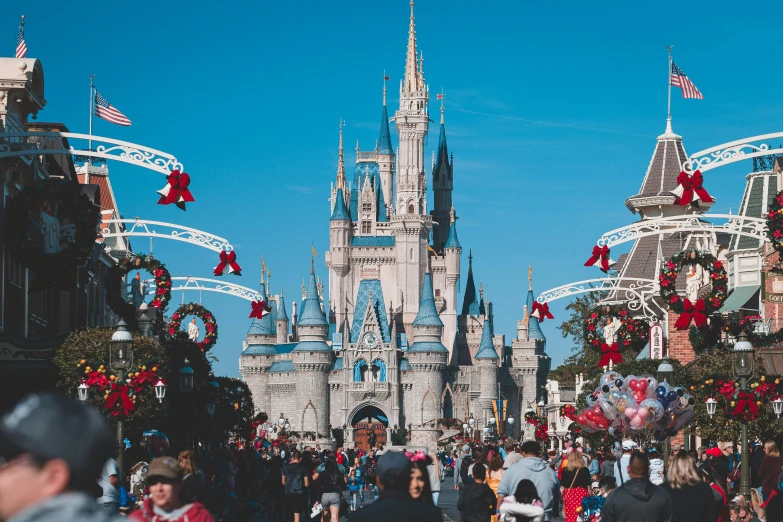 a crowd of people walking down a street in front of a castle, inspired by disney, pexels contest winner, amusement park, holiday season, blue clear skies, thumbnail